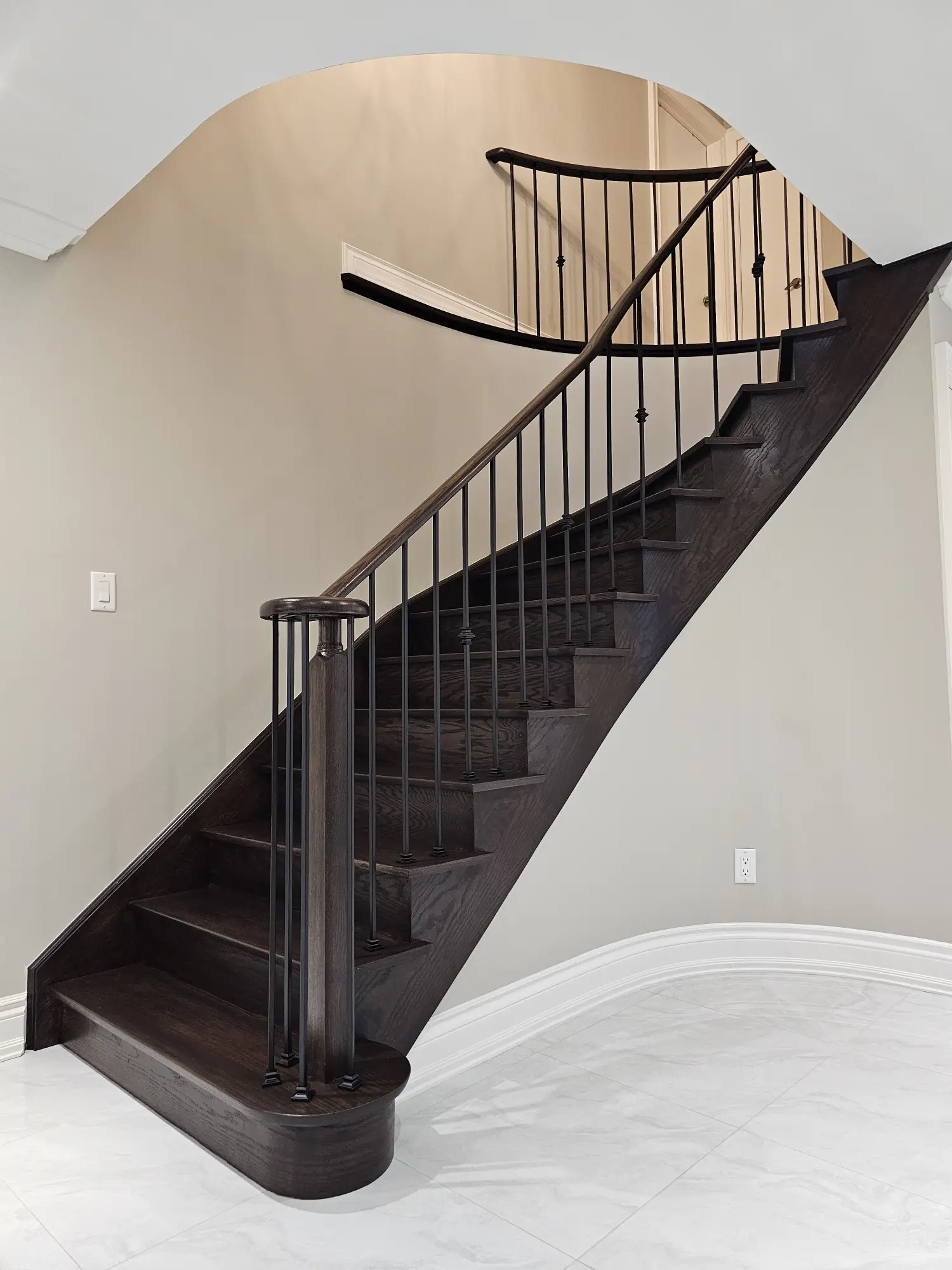Elegant curved staircase refinished with deep-toned hardwood and premium black iron balusters.